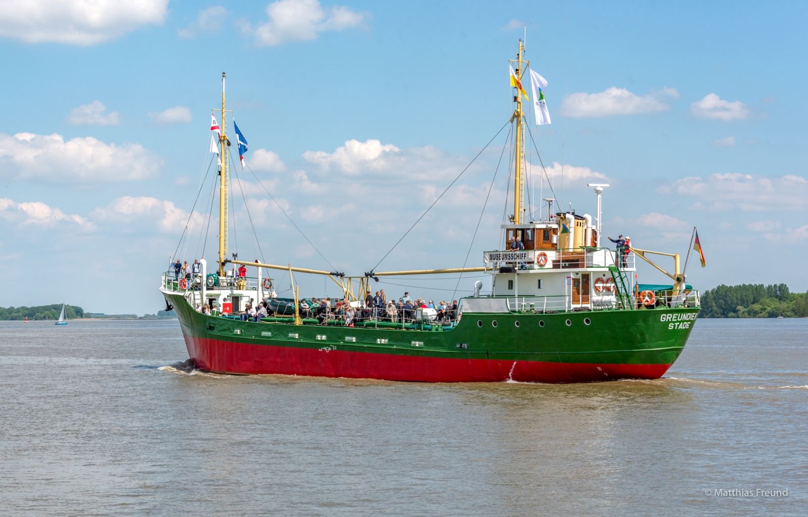 Die MS Greundiek mit grünem Rumpf und Flaggen auf der Elbe
